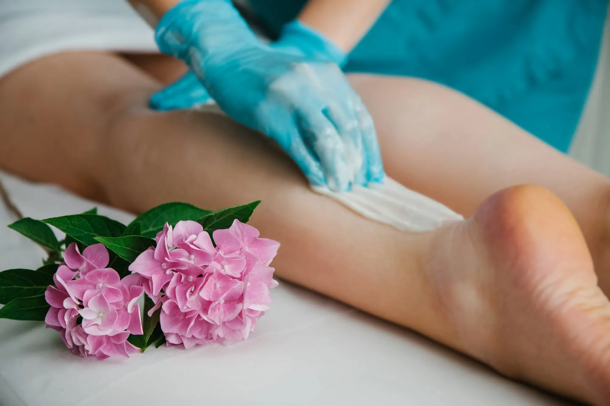 Wax being smoothed onto a leg during a treatment, with pink hydrangeas in the foreground